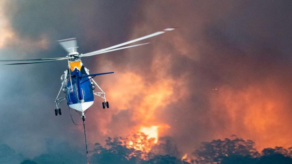 A helicopter flies above flames.