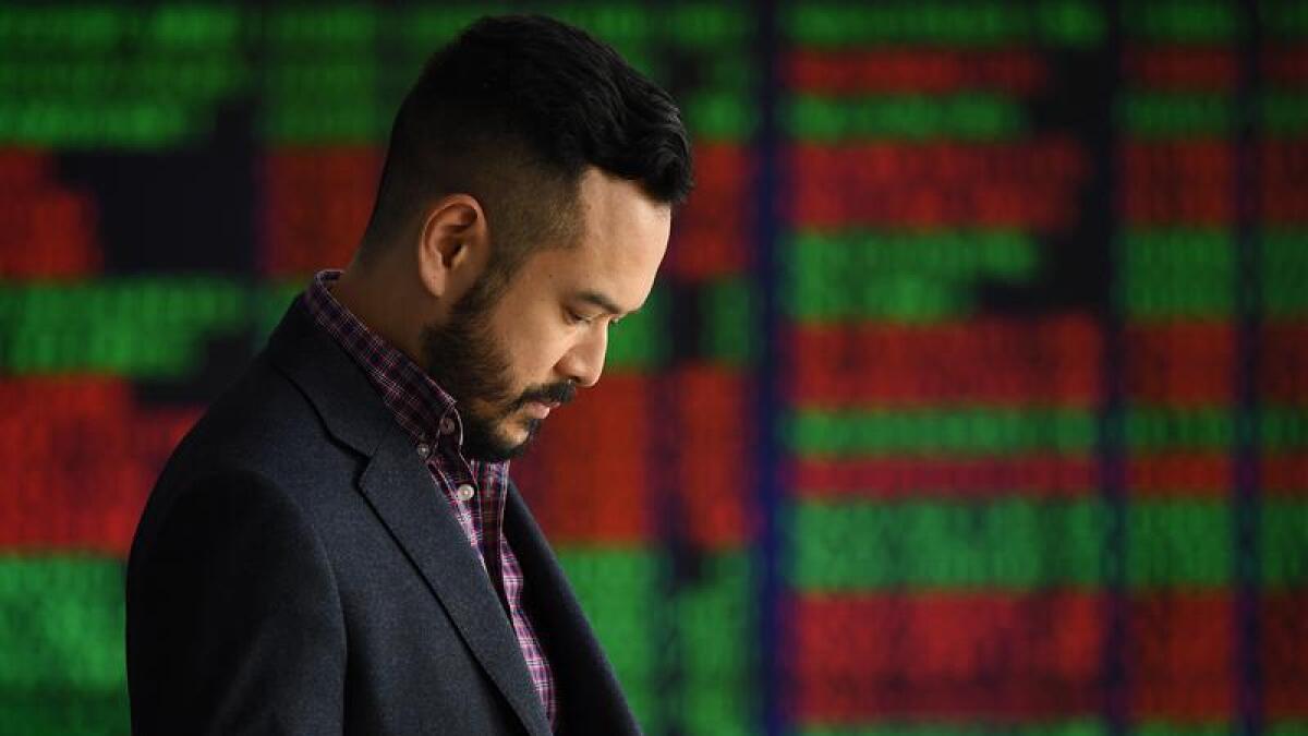 A man stands before an ASX trading display and looks at his phone.