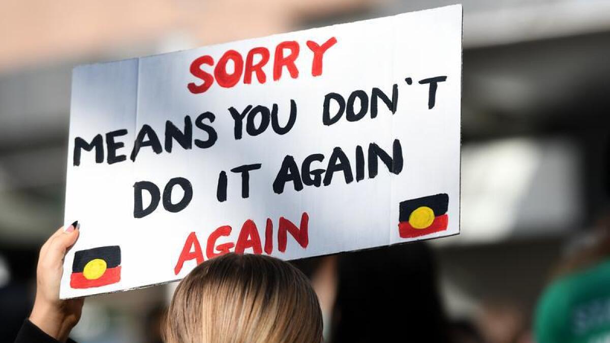 A woman holds up a poster at a Sorry Day march in Sydney in 2021.