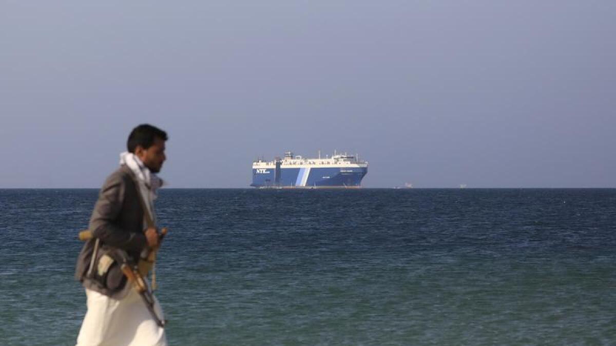Houthi fighter walks on beach with cargo ship in the background