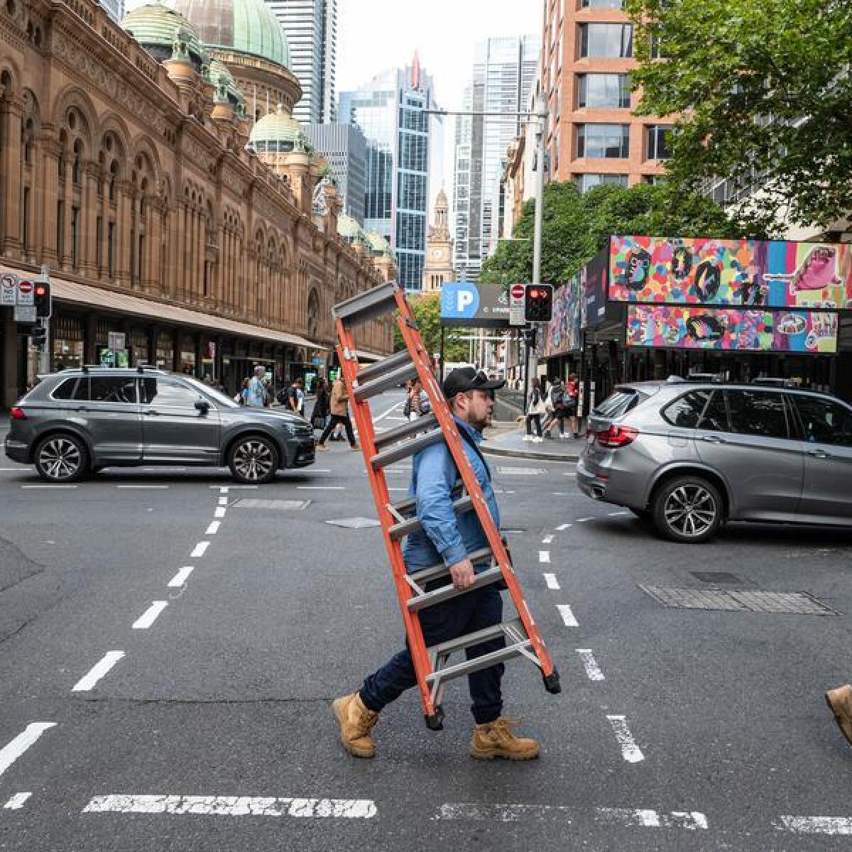 Workmen crossing a road carrying a ladder.