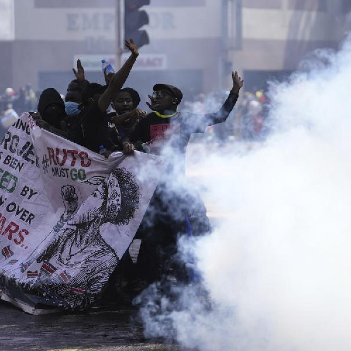 Protesters hide behind a banner as police fire tear gas in Nairobi