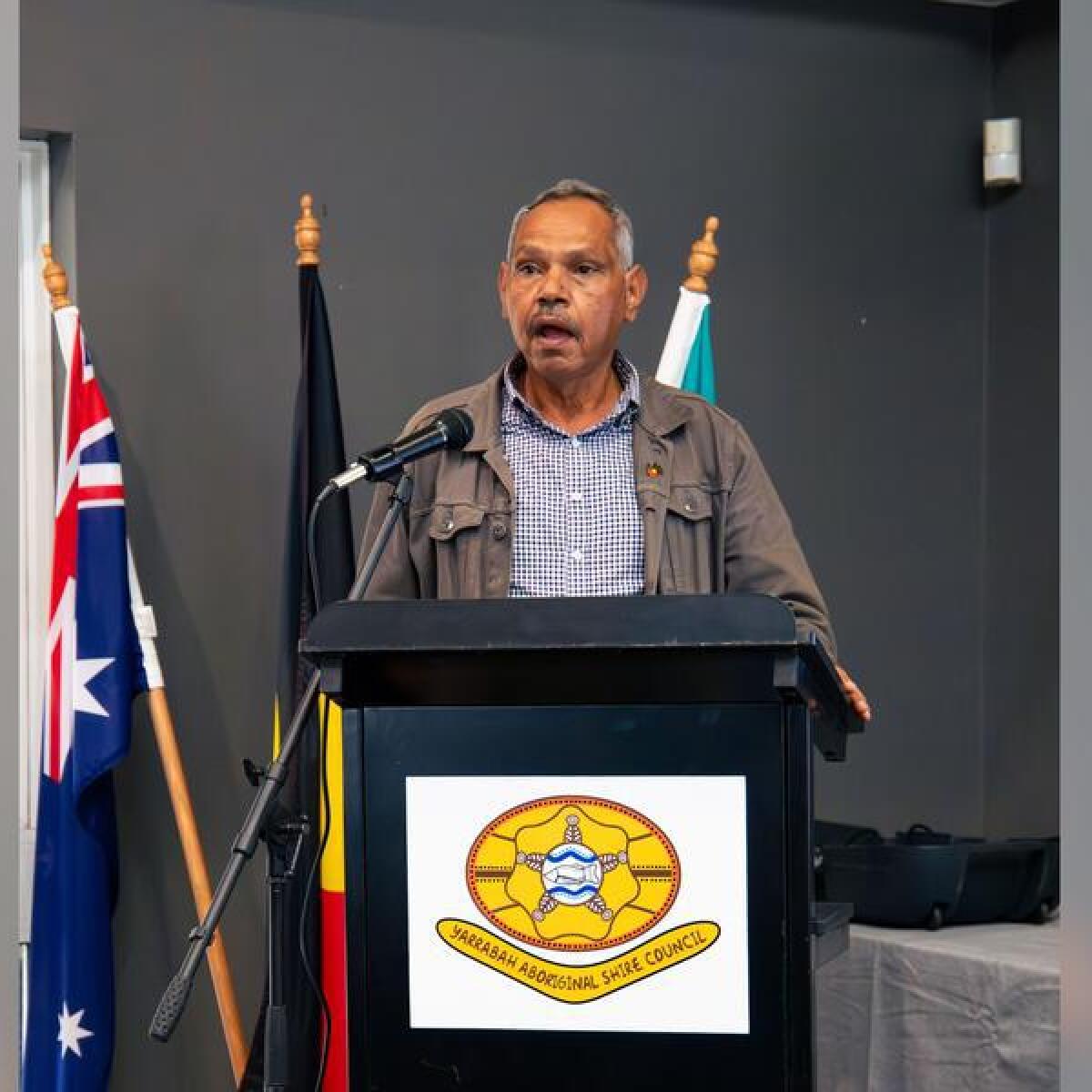 Palm Island Aboriginal Shire mayor Alf Lacey stands at a podium.