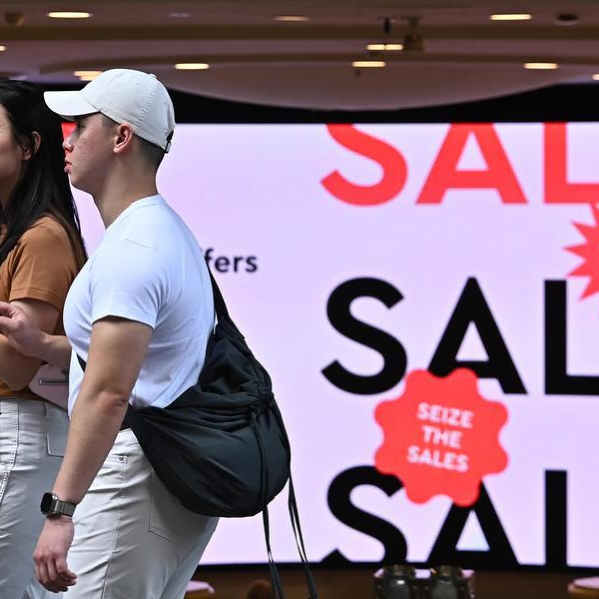 People walk past a sale sign.