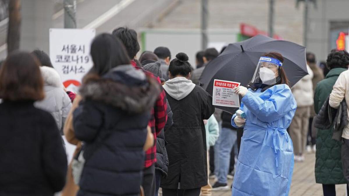 Medical worker holds sign as visitors queue for COVID tests in Seoul..
