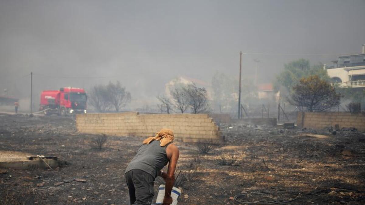 A man drops water on a wildfire near a house in Athens, Greece.