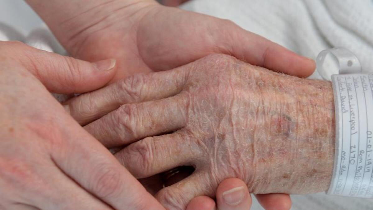 A nurse holds the hand of an elderly patient at Liverpool Hospital