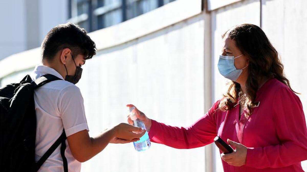 Woman dispenses hand sanitiser to a student at a school.