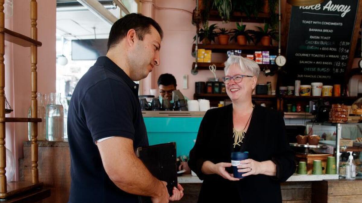 Mohsen holds a clipboard as he chats with Penny Sharpe in a small cafe