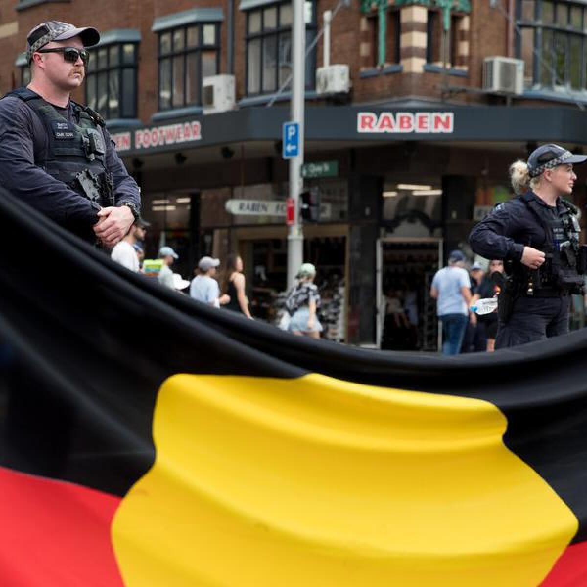 Police officers stand near an aboriginal flag