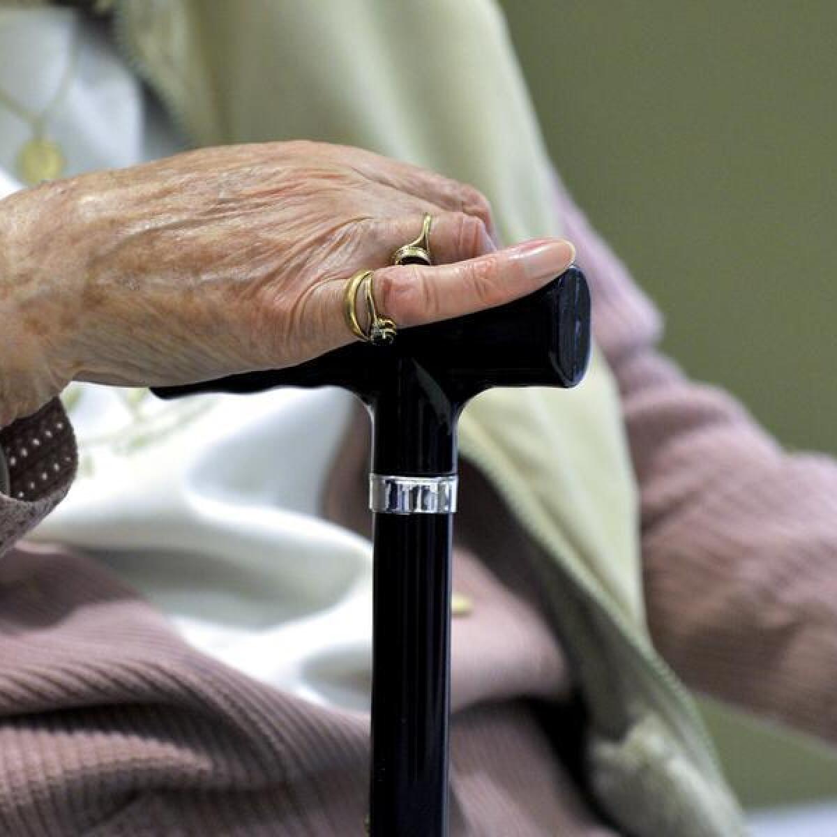 An elderly person holds a walking stick.