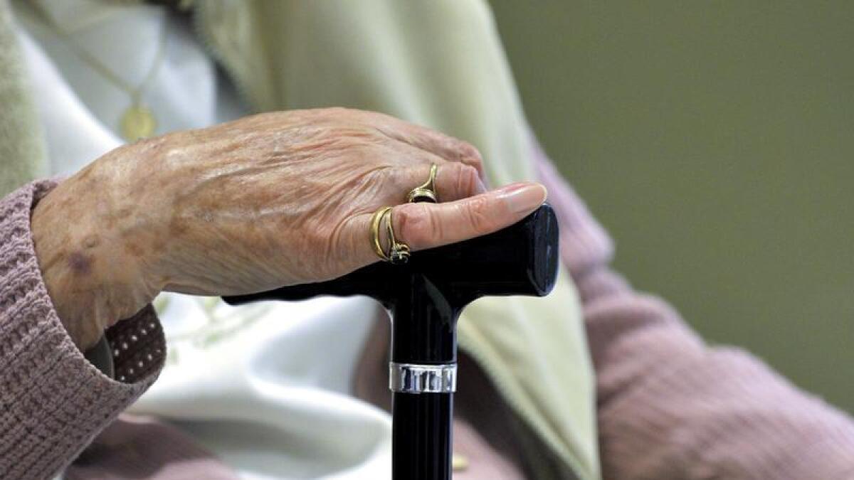 An elderly person holds a walking stick.
