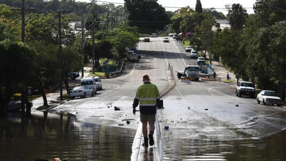 Man walks along a flooded road in Lismore, NSW.