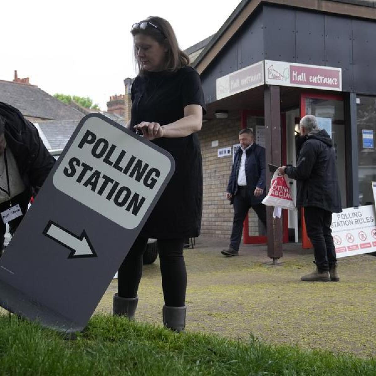 Polling station officials put out a sign as it opens in London
