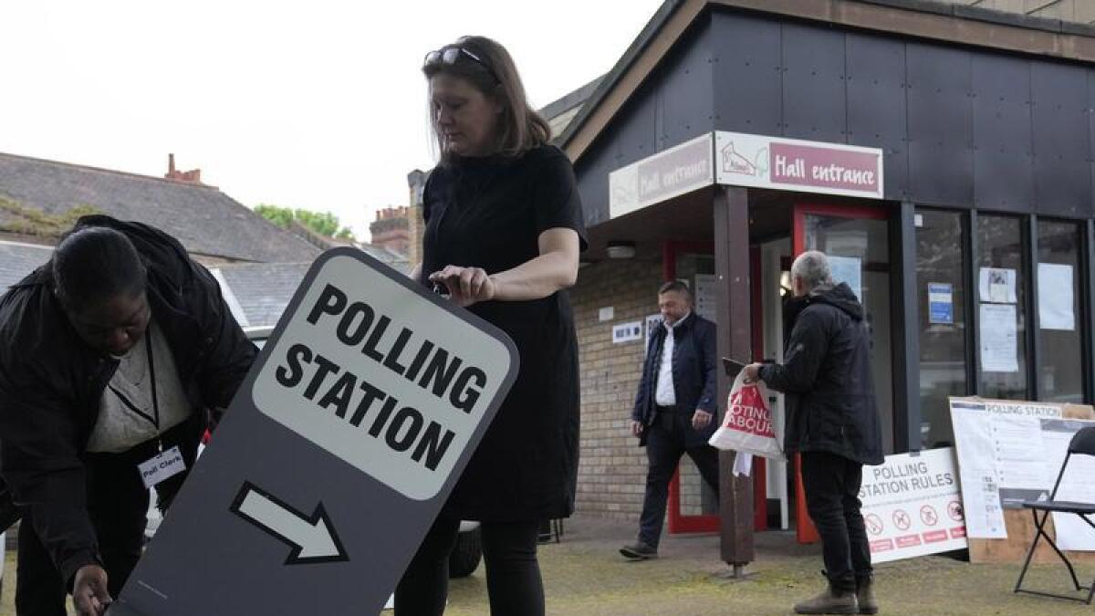 Polling station officials put out a sign as it opens in London