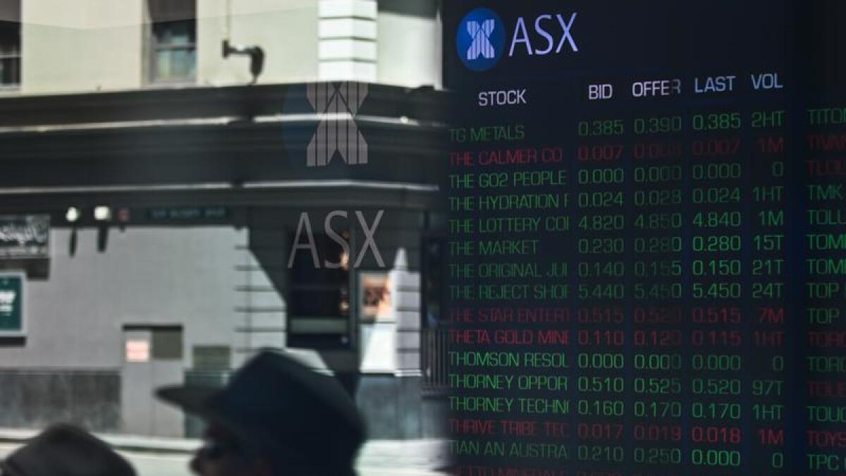 People walking past the ASX share board.