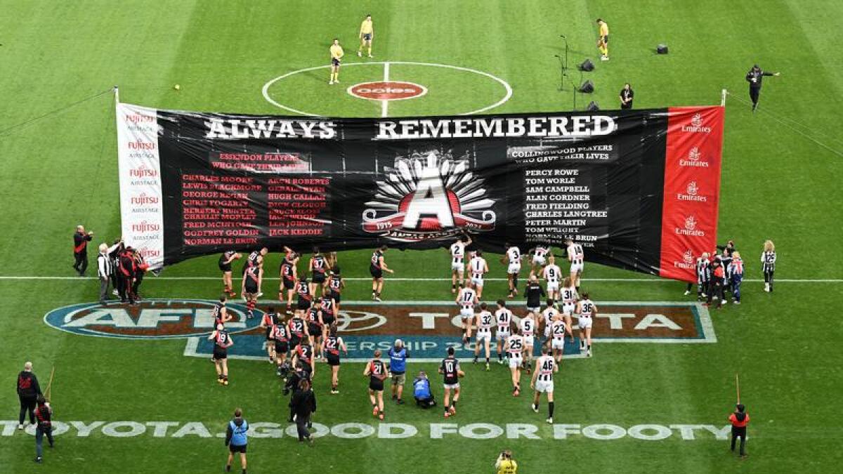 Essendon  and Collingwood players run through the joint banner