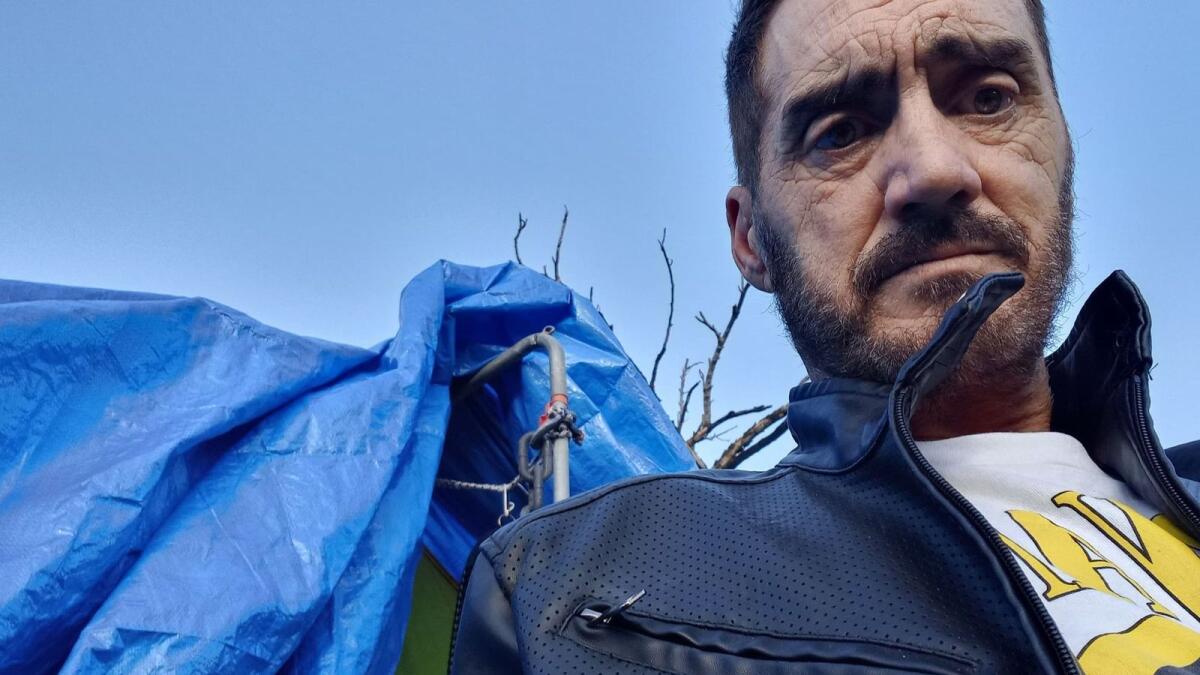 Dion Grahame in front of a blue tarp draped over his tent. 