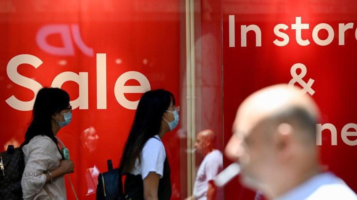 Pedestrians walk past retail signage on a shopfront in Sydney